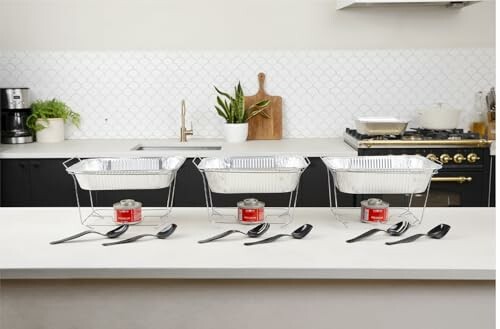 Three chafing dish sets with spoons on a kitchen counter.