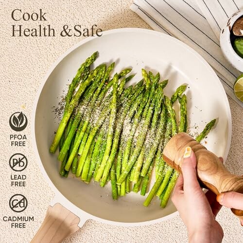Person seasoning asparagus in a white pan with health and safety labels.
