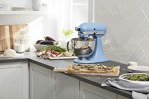 Blue stand mixer on a kitchen counter with vegetables and flatbread.
